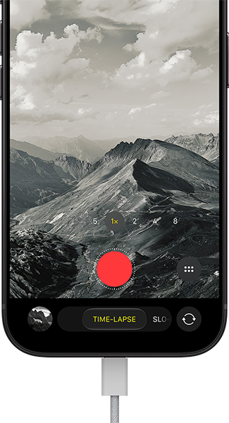 iPhone 18 Pro, front exterior, displaying a mountainous landscape, with the camera mode overlay in Time-Lapse mode, with power cable attached to charging port