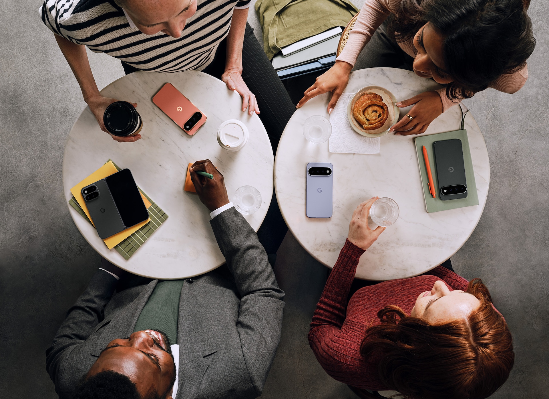An overhead shot of people having a meeting at a cafe, with multiple Pixel 11 phones on the table
