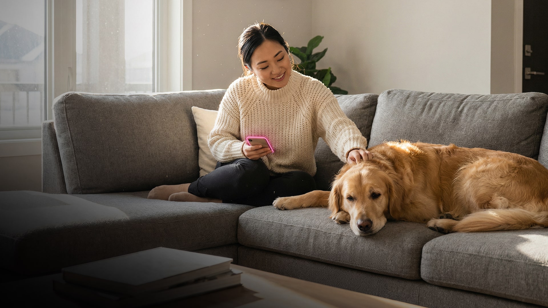 Woman on couch pets her dog and holds her phone with a T-Mobile magenta glow.