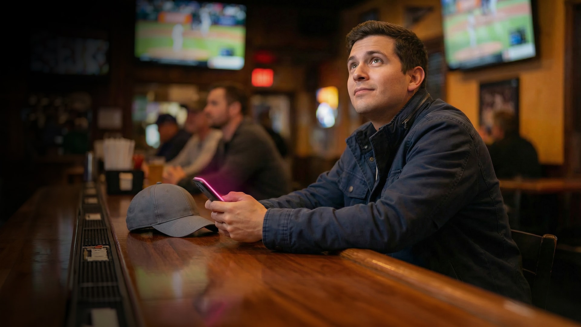 Man in sports bar watches TV and holds his phone with a T-Mobile magenta glow.