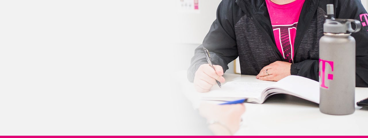 Persona con una camiseta de T-Mobile sentado en una mesa de conferencias y tomando notas durante una reunión