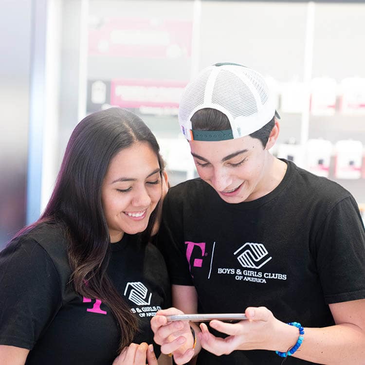 Dos estudiantes usando un smartphone en una tienda T-Mobile.