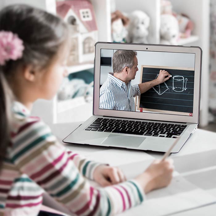 A student watching a teacher on a laptop and taking notes.