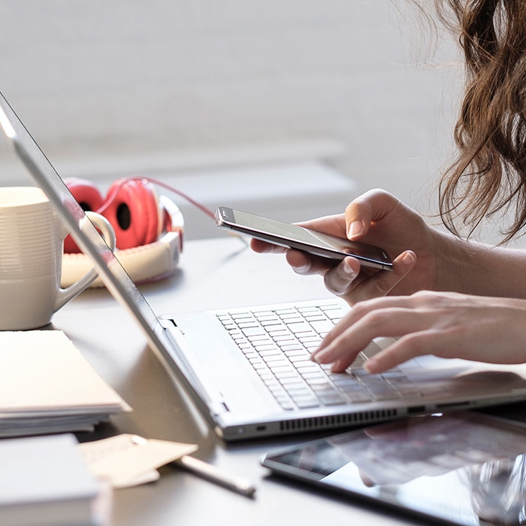 Una mujer usando una computadora y su teléfono.