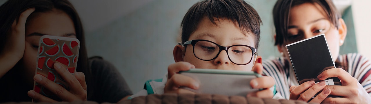 Three kids lying together on a bed, looking at their phones