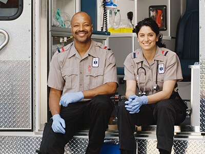 Two first responders in uniform smiling and sitting in an emergency response vehicle