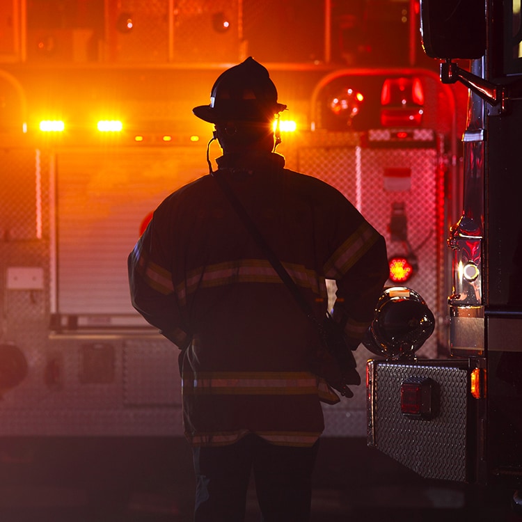 Bombero de pie frente a un camión de bomberos con las luces encendidas