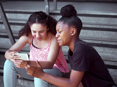 Two kids sitting on steps and looking at a phone while smiling.