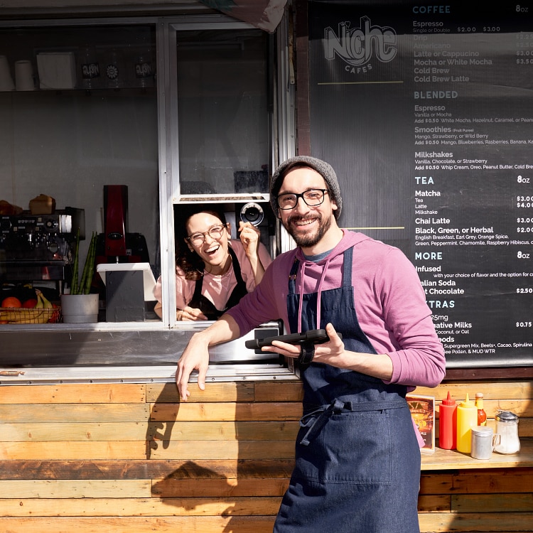Cheerful man and woman at the order window of their coffeeshop food truck. Man is holding a tablet.