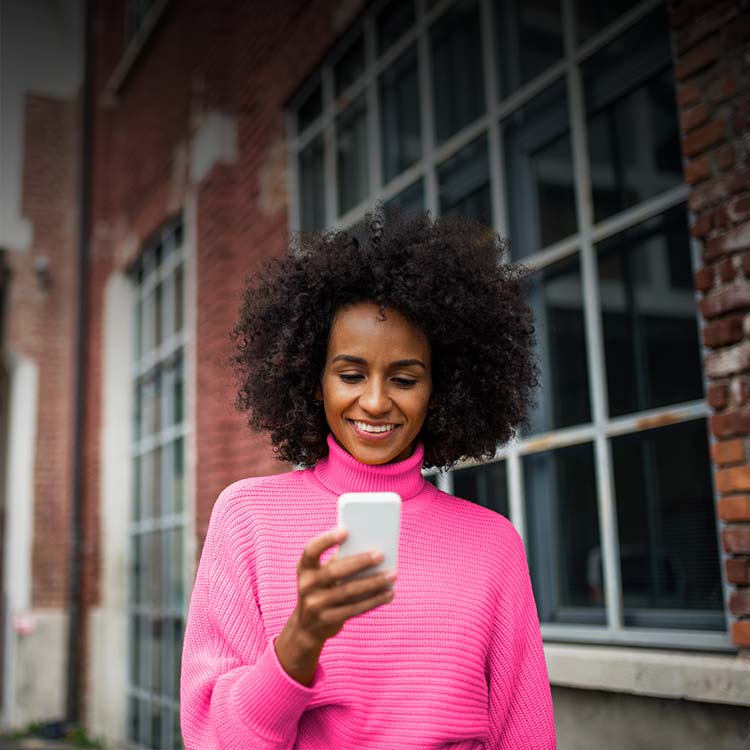 Woman outside in a magenta turtleneck smiling while looking down at her phone