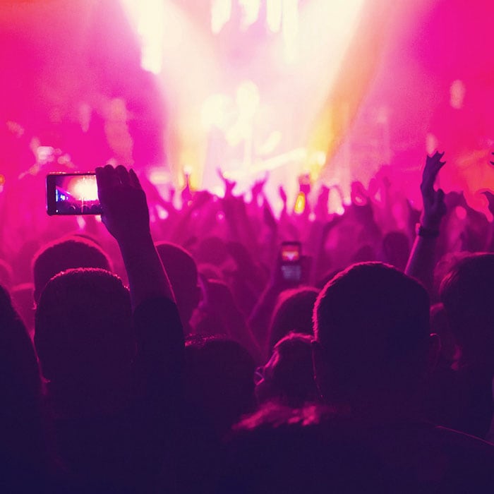 Fans in a concert crowd holding their phones up for photos