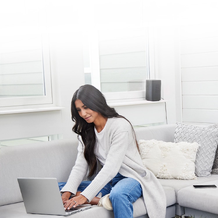 A woman sitting on a bed looks down at a laptop. 