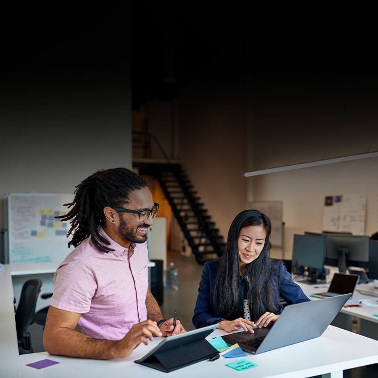 A man and a woman smile while working side by side in an office.
